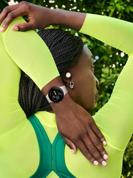 A person wearing neon yellow clothing, Pixel Buds and a Pixel Watch stretches their arm behind their back.